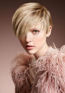 A young women dressed in blush pink osterich feathers showcases her blonde pixie.